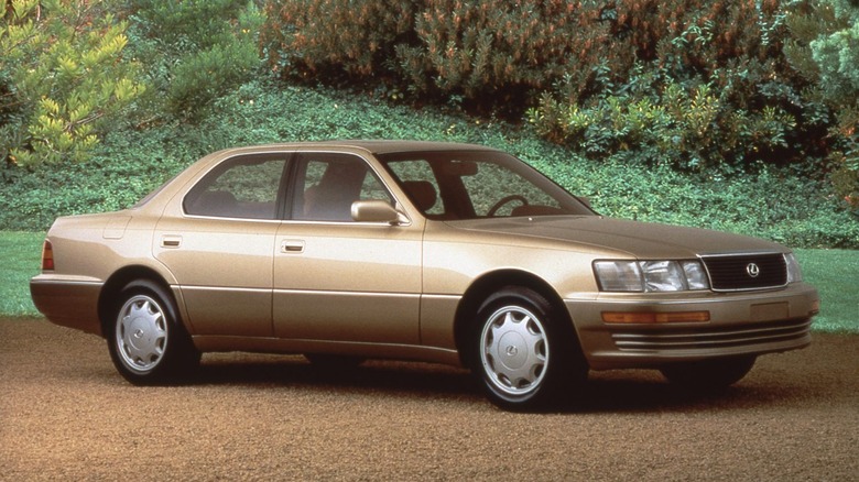 A gold-colored 1993 Lexus LS 400 parked on gravel in front of greenery.