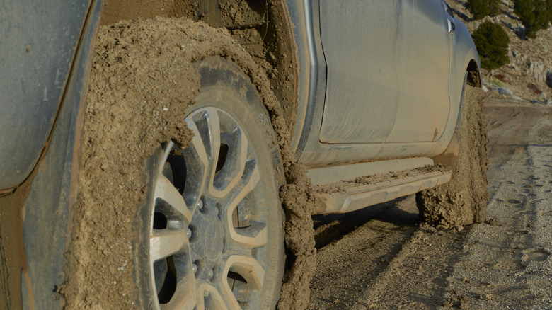 Rear lower quarter view of a pickup truck forging a rough road and with tires wrapped in mud