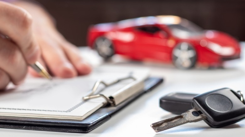 a personification signing paperwork for a caller car pinch keys successful nan foreground and a artifact car successful nan background