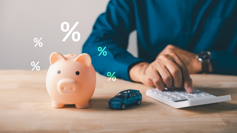 A man shops for car insurance using a calculator. A small piggy bank sits on the desk in front of him.