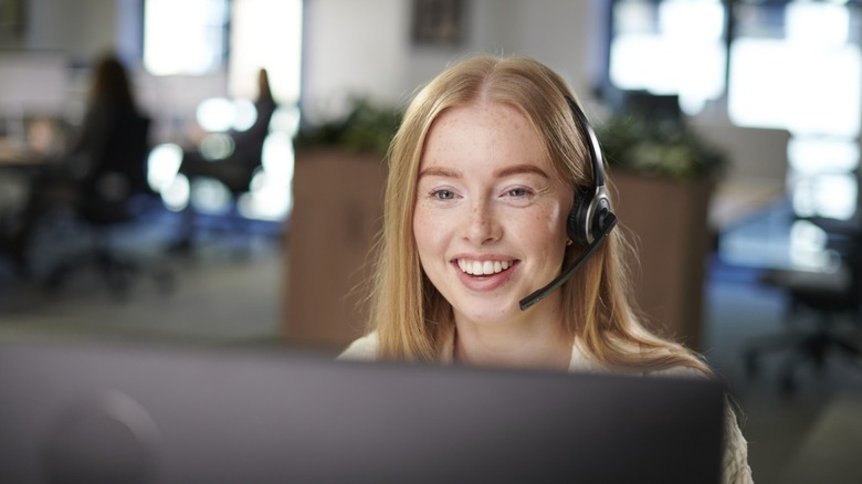 A customer service representative in a call center, wearing a headset and looking at a computer screen