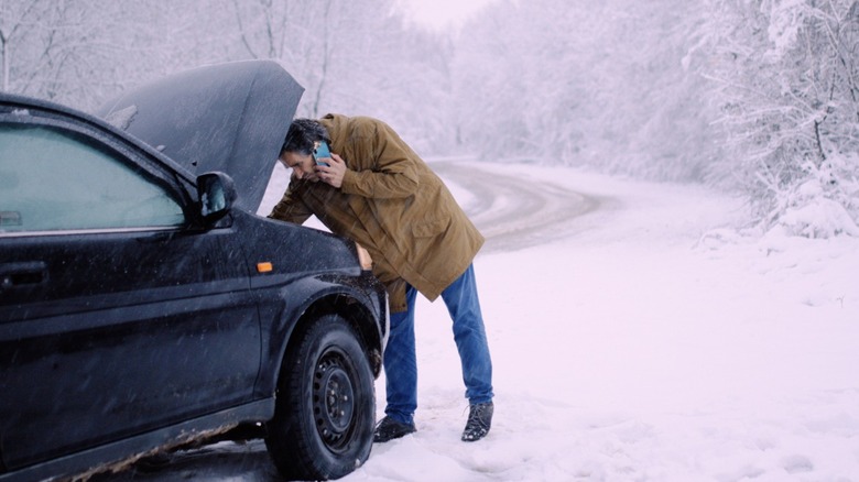 A man trying to fix a stalled car in a snowy blizzard