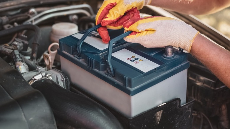 A person in gloves removing a car battery
