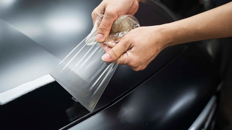 A technician removing old paint protection film from a car in a garage