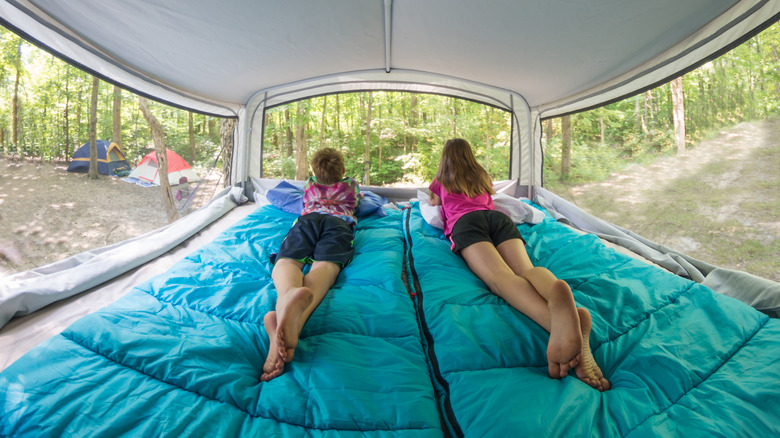 Kids laying on sleeping bags on a bed in a pop-up camper