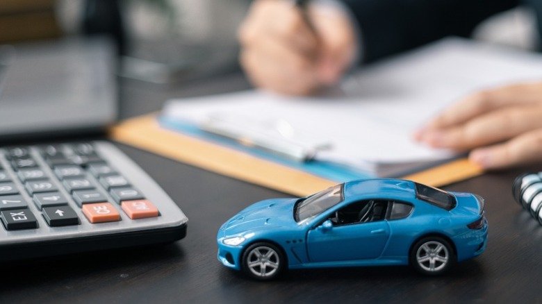 A toy car in the foreground, with a person signing paperwork in the background.