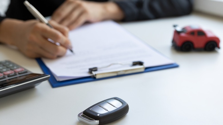 A person signing a contract with a toy car nearby on the desk.