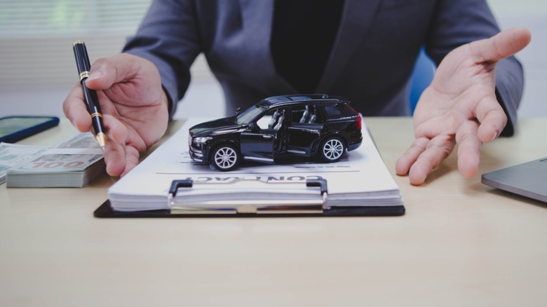 A toy car on top of a contract on a clipboard.