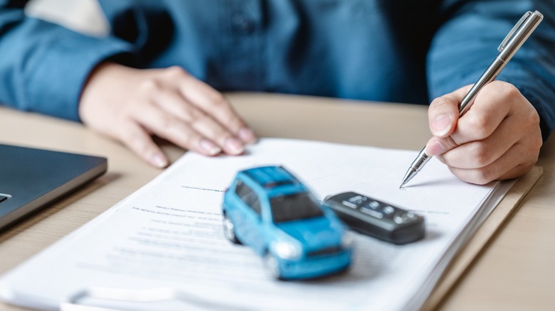 A person signing a contract with a toy car on top of the paperwork.