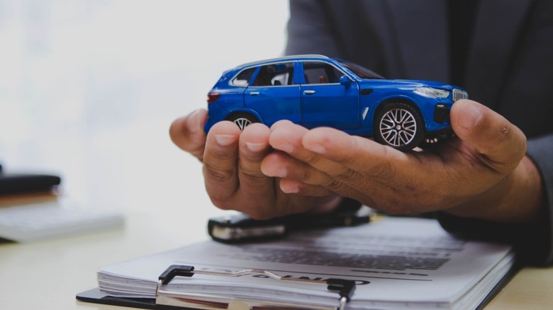 A man's hands holding a blue toy car over a contract
