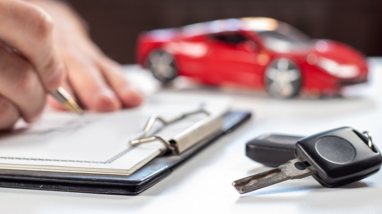 Car keys in the foreground, a person signing paperwork in the middle distance, and a toy car in the background.