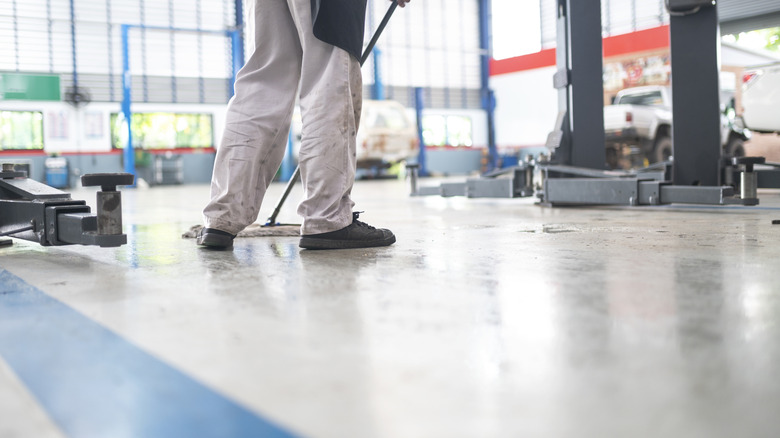 A person cleaning a garage floor near a four-post lift