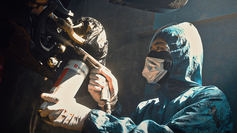 A technician applying rubberized coating to the undercarriage of a vehicle