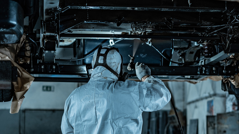 A technician applying undercoating to a lifted vehicle
