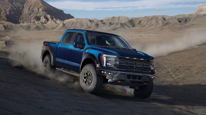 The passenger-side front 3/4 of a 2025 Ford F-150 Raptor R kicking up dirt in the desert