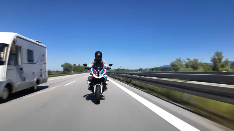 A lone rider on the highway with a European RV passing on his right, camera left.