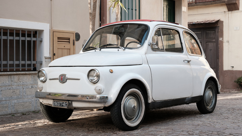 A classic Fiat 500 parked on a historic cobblestone road