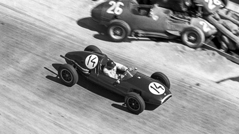 Jack Brabham drives a rear-engine Cooper T43 racecar past the wreckage of two front-engine cars