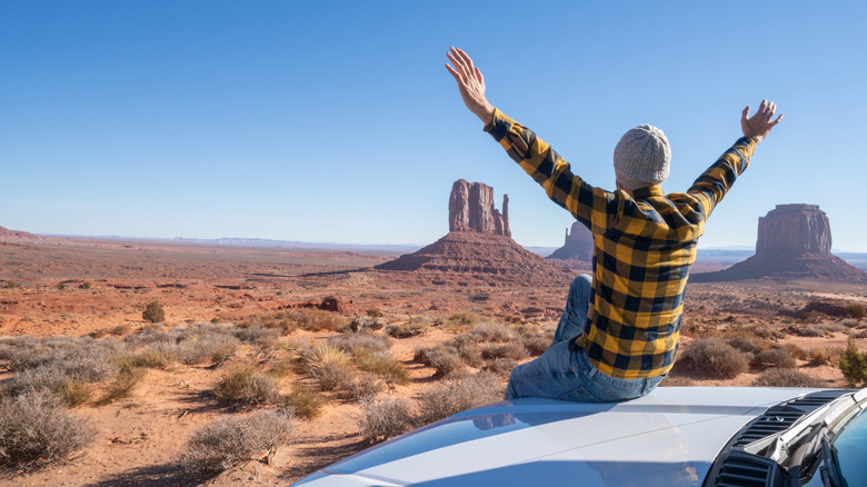 A man on a road trip sitting on the hood of his car in the desert