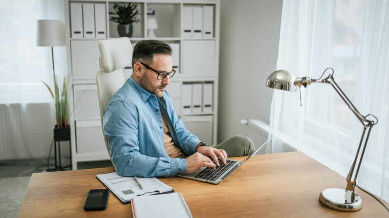 A lightly-bearded man looks something up on a laptop computer.