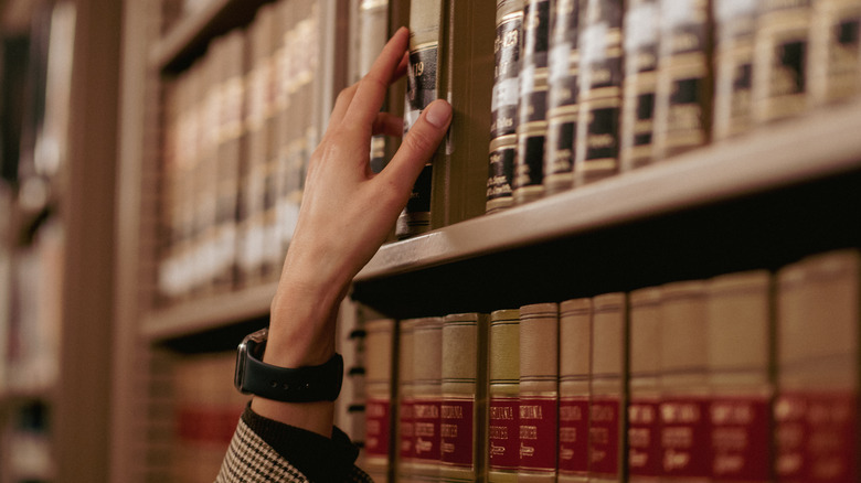 A hand reaches up to take a law book off of a shelf.