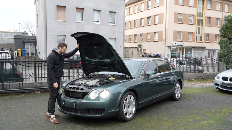 A green Bentley Flying Spur with the hood open and a man looking at the engine