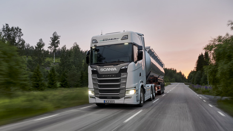 A front 3/4 view of a Scania Super semi truck with a tanker trailer on a road