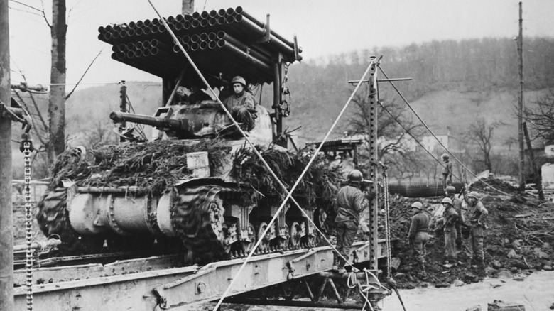 A black and white image shows a Sherman tank with a Calliope rocket system on a deployable bridge in Germany