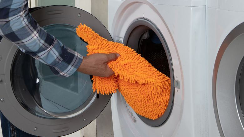 A person placing an orange microfiber towel in the washing machine