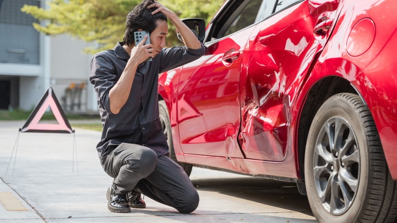Man knelt down next to car after accident, making a phone call