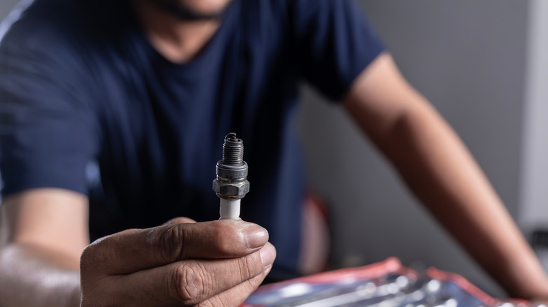 A mechanic holding up a worn-out spark plug from a car engine