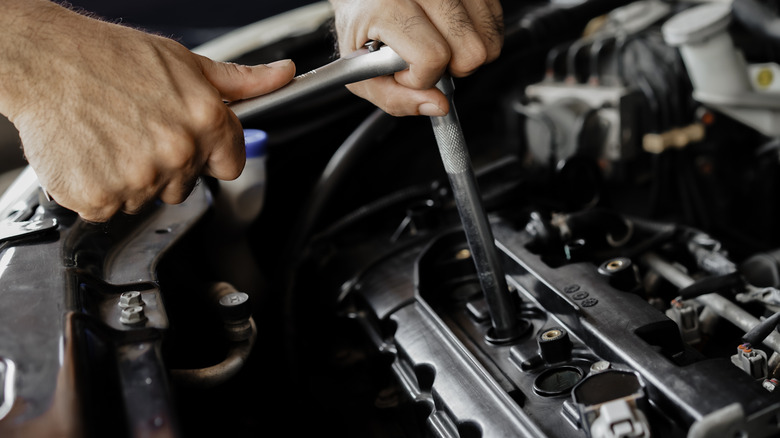 Mechanic using a socket wrench and a spark plug socket to loosen the plugs