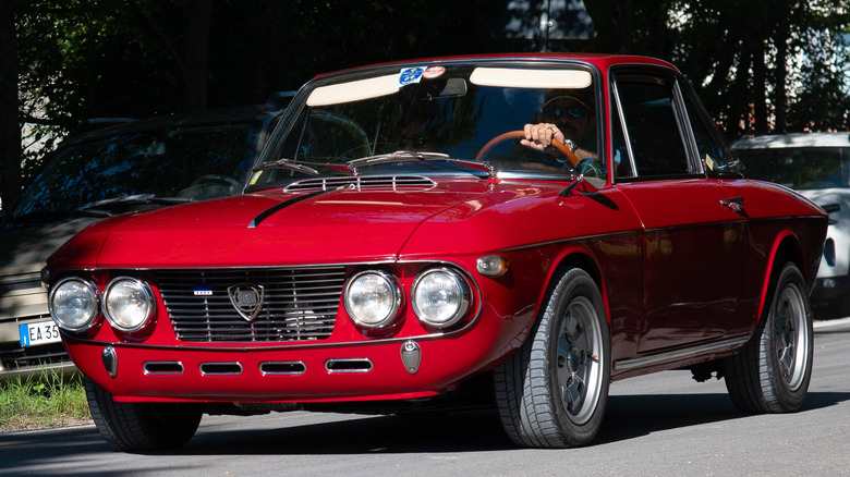A red Lancia Fulvia Coupe driving down the road.