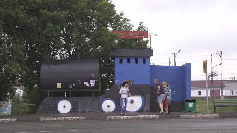 Train-shaped bus stop with people waiting for a bus.