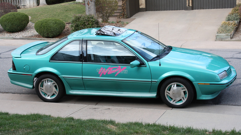 A teal 1990 Chevy Beretta Indy Pace Car replica parked next a lawn