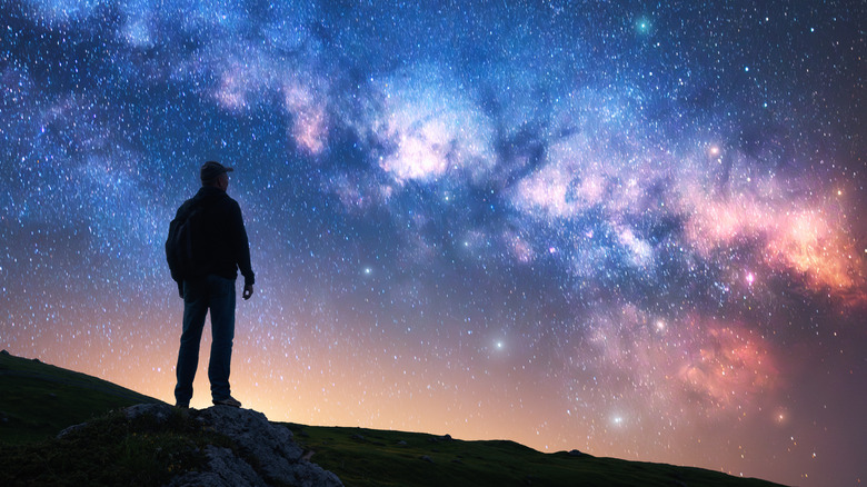 Silhouette of a person atop a hill gazing out at the Milky Way galaxy