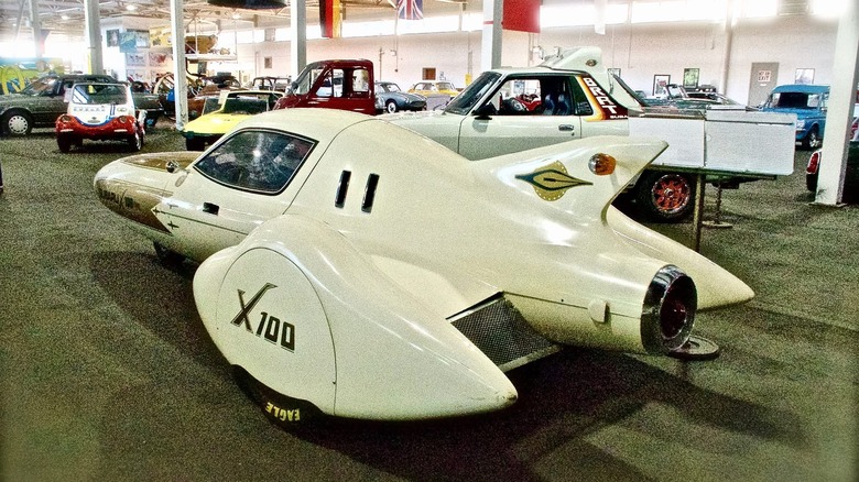 Rear 3/4 view of the Subaru X-100 concept car with a Subaru BRAT and other cars in the background
