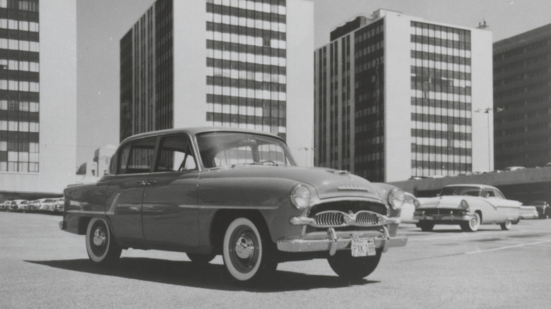 A 1958 Toyota Toyopet Crown, the first Toyota imported into the U.S. parked in a parking lot in downtown Los Angeles in front of three high-rise buildings and other cars
