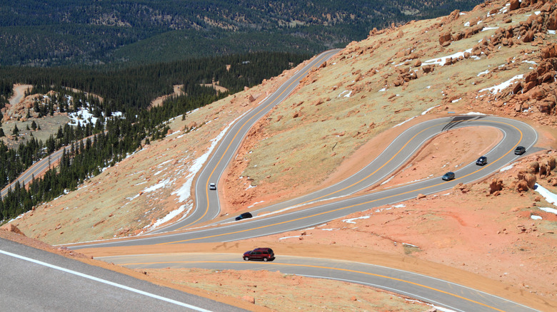 A scenic shot showing the twists and turns of Pikes Peak Highway with multiple cars driving