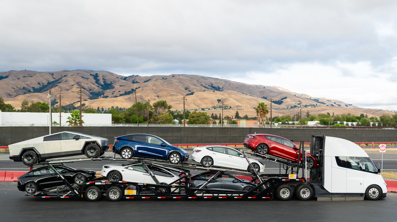 A side view of a Tesla Semi towing a car carrier filled with Teslas parked in front of a mountain