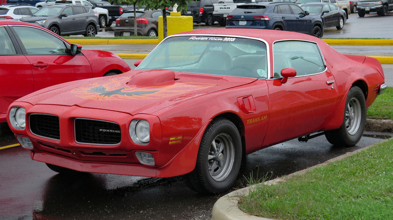 A red 1973 Pontiac Firebird Trans Am in a wet parking lot