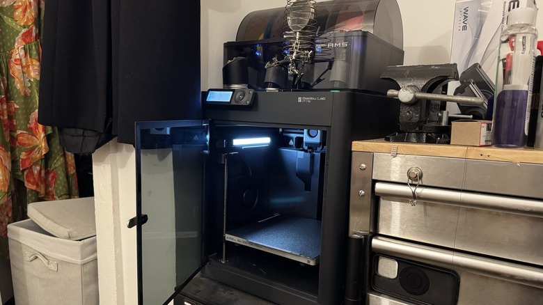 Amber's 3D printer with solder supplied stacked atop, next to her messy workbench