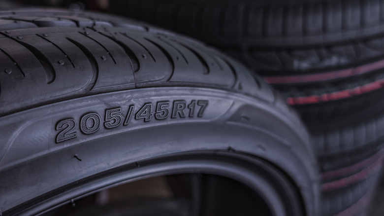 A closer view of the sidewall of a tire with the size marking and with stacked tires in the background