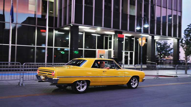A vintage yellow car cruises down the street.