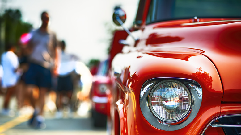 A vintage red auto is in the foreground as people walk in the background.