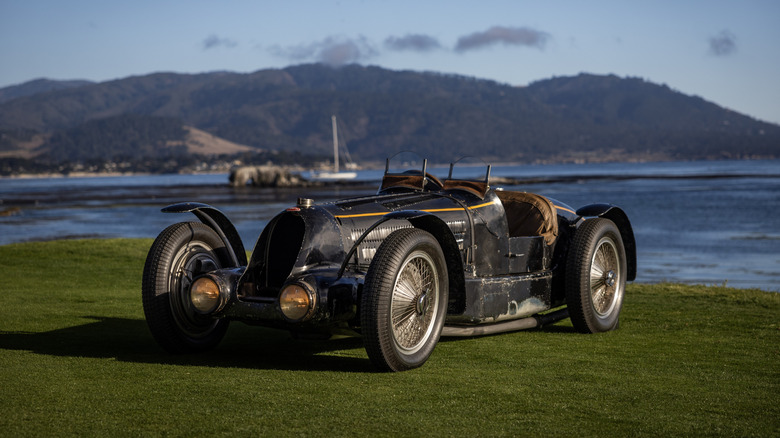 A vintage Bugatti parks near the water.