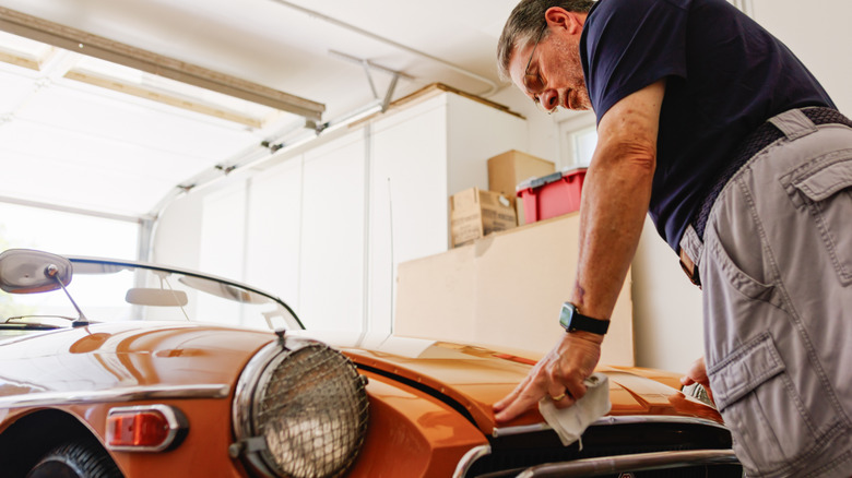 A senior man standing over a vintage car in a garage while closing its hood.