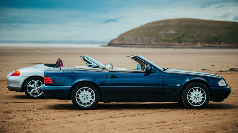 An old Mercedes roadster and an old Porsche parked on a beach.