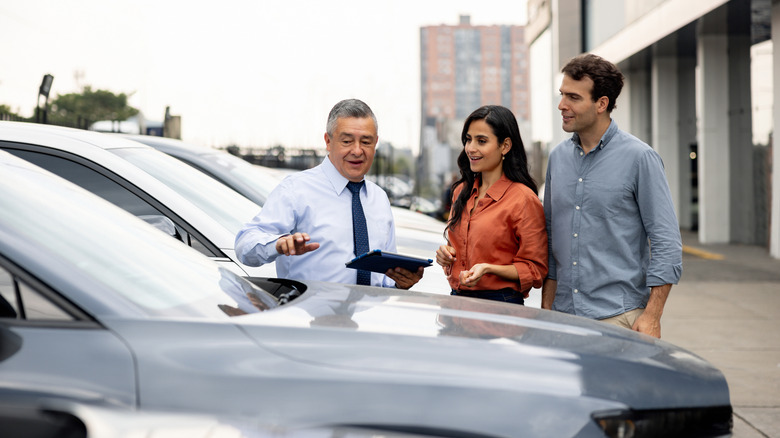 A salesman talks to a couple as they inspect a vehicle