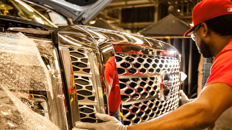 A worker adjusts the grille of a Nissan Titan in a factory.